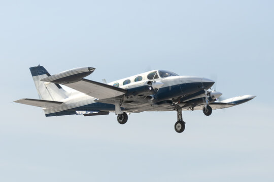 Twin Engine Aircraft during climb out.  Blue and white multi with retractable gear and two propellers departs the airfield for bluer skies. Isolated airplane flying overhead