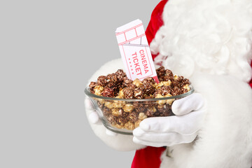 Santa Claus with bowl of sweet popcorn and cinema tickets on grey background. Closeup