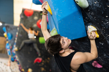 young muscular male sportsman climbing black wall for bouldering in gym