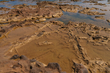 Detailed view of a coastal rock surface displaying natural erosion patterns and shallow tidal pools. The rugged terrain showcases the geological features of the shoreline