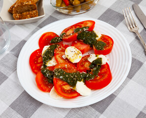 Italian style salad Caprese with fresh tomatoes and tender mozzarella dressed with fragrant sauce pesto and sesame seeds..