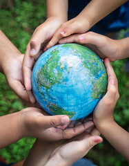 Group of children holding planet earth over defocused nature background with copy space
