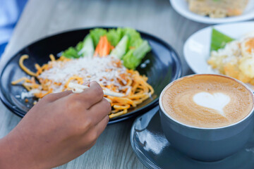 a portrait of a hand holding chopsticks to pick up pasta on a plate and a latte with a heart-shaped topping