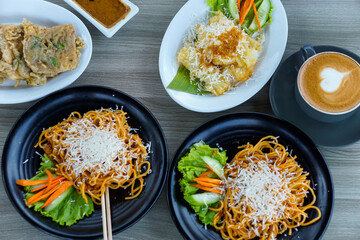 A delicious spread of noodles, fried snacks, and coffee served on a wooden table.
