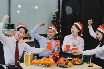 full length view of a group of business team wearing red Santa hat and exchange gift box together in the office for Christmas.