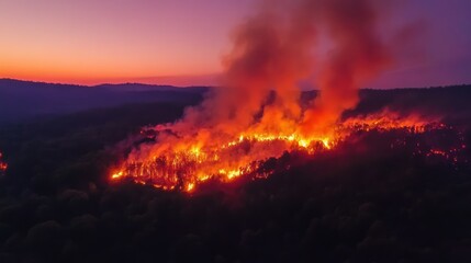 Aerial view of a forest fire at sunset, showcasing flames and smoke in a natural landscape.