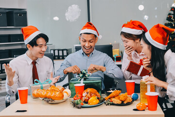 full length view of a group of business team wearing red Santa hat and exchange gift box together in the office for Christmas.