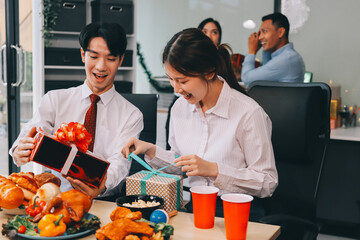 full length view of a group of business team wearing red Santa hat and exchange gift box together in the office for Christmas.