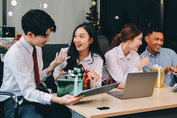 full length view of a group of business team wearing red Santa hat and exchange gift box together in the office for Christmas.