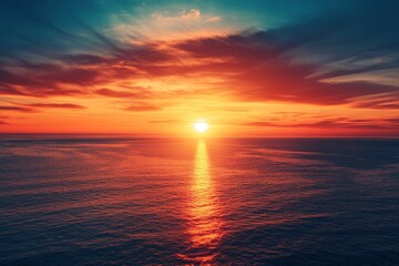 Obraz premium Dramatic orange sunset reflecting off a calm ocean with a blue sky above.