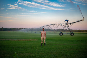 Farmer near Irrigation system is watering large alfalfa field. Man with Automatic Sprinkler irrigation system watering farm field. Sprinkler Irrigation system watering a lawn. Agriculture irrigation.
