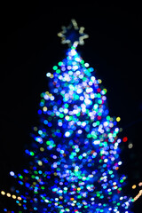 Christmas tree holiday with snowflake topper background. Decorated Christmas Tree. Blurred Christmas tree at night. festive Christmas tree with lights garlands. The first star lit up.