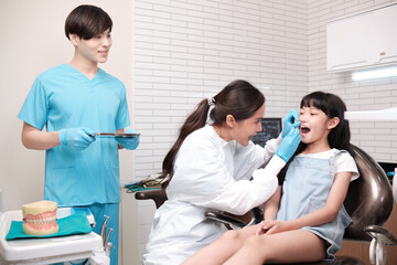 Fototapeta premium Asian female pediatric dentist and assistant check and examination a little girl's caries teeth in dental clinic, well-being hygiene, and professional orthodontic healthcare work in kid hospital.