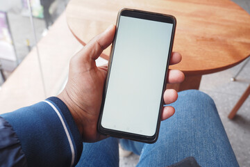 A person sits in a cozy cafe, holding a smartphone with a blank screen, hinting at engagement