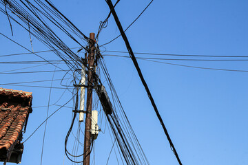 A close-up shot of a utility pole with an abundance of tangled wires against a bright blue sky....
