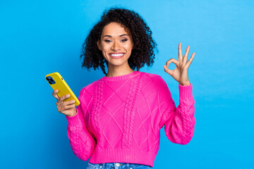 Photo of nice young girl hold smart phone show okay symbol wear pink sweater isolated on blue color background