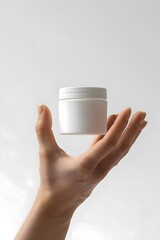 product photography of a hand holding a white cosmetic jar against a white background