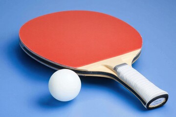 A red and black table tennis paddle and a white ball on a light blue background.