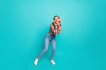 Full length photo of charming positive woman wear print shirt dancing enjoying song earphones empty space isolated teal color background