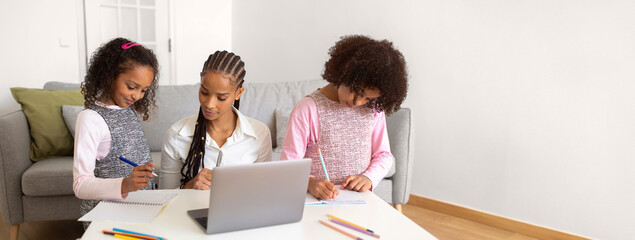 African American mother assists her two daughters with their homework in a comfortable living room, surrounded by colorful stationary and a laptop on the table as they focus on their tasks.