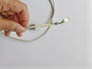 Old charger cable broken, close-up of broken white insulation. Faulty charging cord, device...