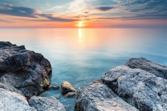 Serene sunrise over tranquil ocean with rocky shoreline.