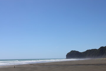 gentle ocean waves roll ashore onto black sand beach under clear blue skies