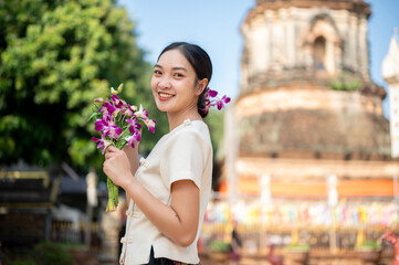 A charming Asian woman in a traditional dress smiling at the camera with a pagoda in the background.