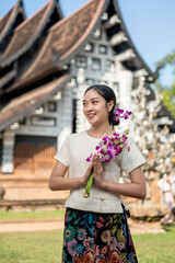 Charming Asian woman in a traditional Thai Lanna dress stands in front of a beautiful ancient temple