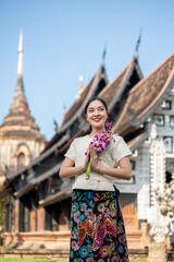 Charming Asian woman in a traditional dress stands outdoors with an ancient temple in the background