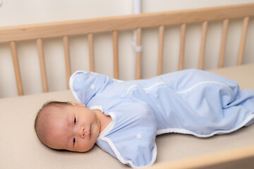 Newborn baby with swaddled wrapped and lying on bed