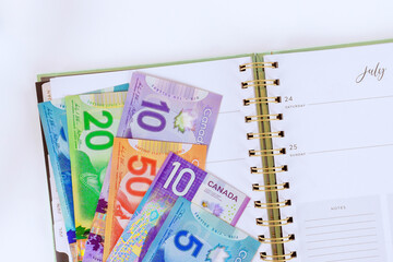 Organize Canadian dollar banknotes cash bills in calendar planner for financial planning.