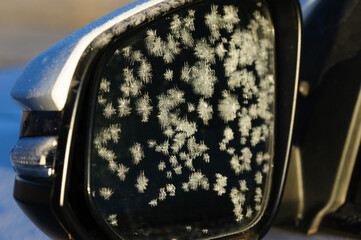 Frost icy flowers on a winter car rear view mirror