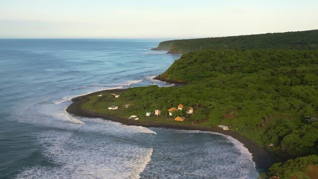 El Salvador Punta Mango beach panoramic aerial view of small shacks and huts surrounded by green nature foliage and waves during early morning - Drone Orbit