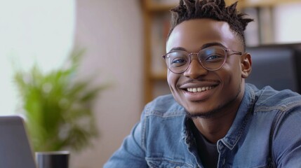Naklejka premium A man with glasses is smiling and sitting at a desk with a laptop