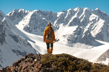 Woman hiker is standing with small backpack and hiking poles high in mountains and looks at white glacier