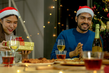 Group of Asian friends enjoying Christmas party for new year celebrate. Friends having fun together at home. men and women opening box gift and present together at home with Christmas tree.
