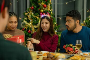 Group of Asian friends enjoying Christmas party for new year celebrate. Friends having fun together at home. men and women opening box gift and present together at home with Christmas tree.