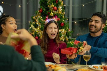 Group of Asian friends enjoying Christmas party for new year celebrate. Friends having fun together at home. men and women opening box gift and present together at home with Christmas tree.