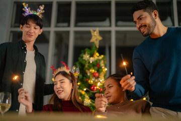 men and women holding sparkler fireworks in a party with Christmas tree. young couple Asian people enjoy celebrating Christmas and New Year. happy and celebrate with food wine and friendship for love,