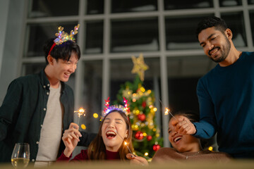men and women holding sparkler fireworks in a party with Christmas tree. young couple Asian people enjoy celebrating Christmas and New Year. happy and celebrate with food wine and friendship for love,