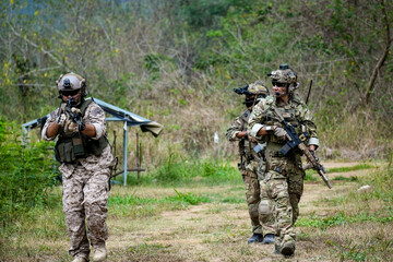 A group of military men in combat gear patrol in the middle of a desert and tropical jungle. Soldiers in full combat gear in dry weather conditions assemble and march on a mission.