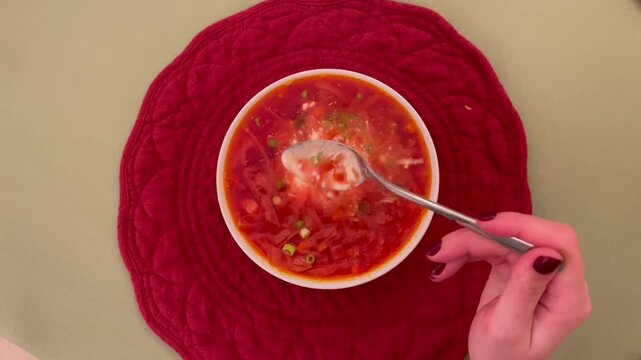Hand stirring sour cream into vibrant red borscht soup.