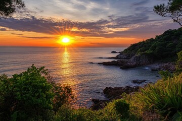 Obraz premium A vibrant sunset over the ocean, casting a warm glow on the rocky coastline.