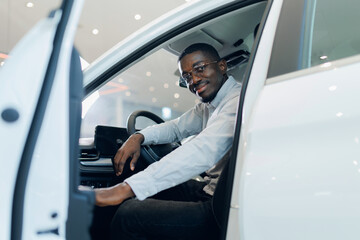 Young African American man sits in driver seat and buying new car and hold key