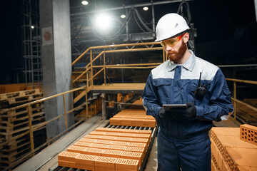 Portrait man worker holding tablet computer for control quality of bricks. Production line of ceramics factory