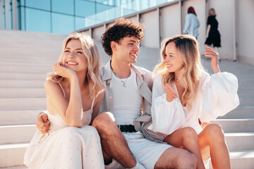 Young three stylish friends posing in the street. Fashion man and two cute female dressed in casual summer clothes. Smiling models having fun. Cheerful women and guy outdoors, in sunny day, at stairs