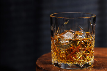 A whiskey glass resting on a wooden table, set against a dark background