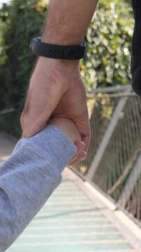 Padre e figlio che si tengono per mano camminando. Primo piano delle mani.
Pap&agrave; che conduce il figlio per mano. Concetto di famiglia, fiducia, protezione, cura, genitorialit&agrave;.