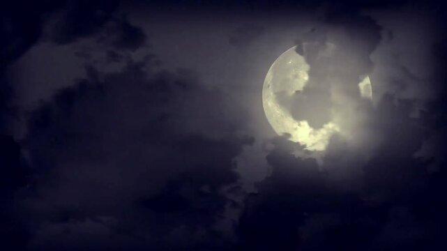 Full moon partially obscured by dark, atmospheric clouds.